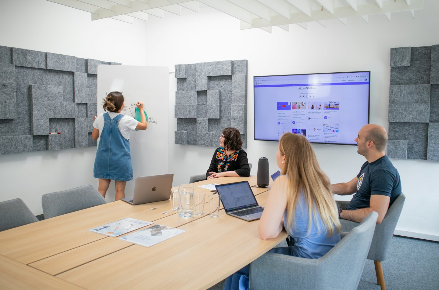 Une équipe collabore autour d'une table et d'un tableau blanc dans un bureau lumineux.