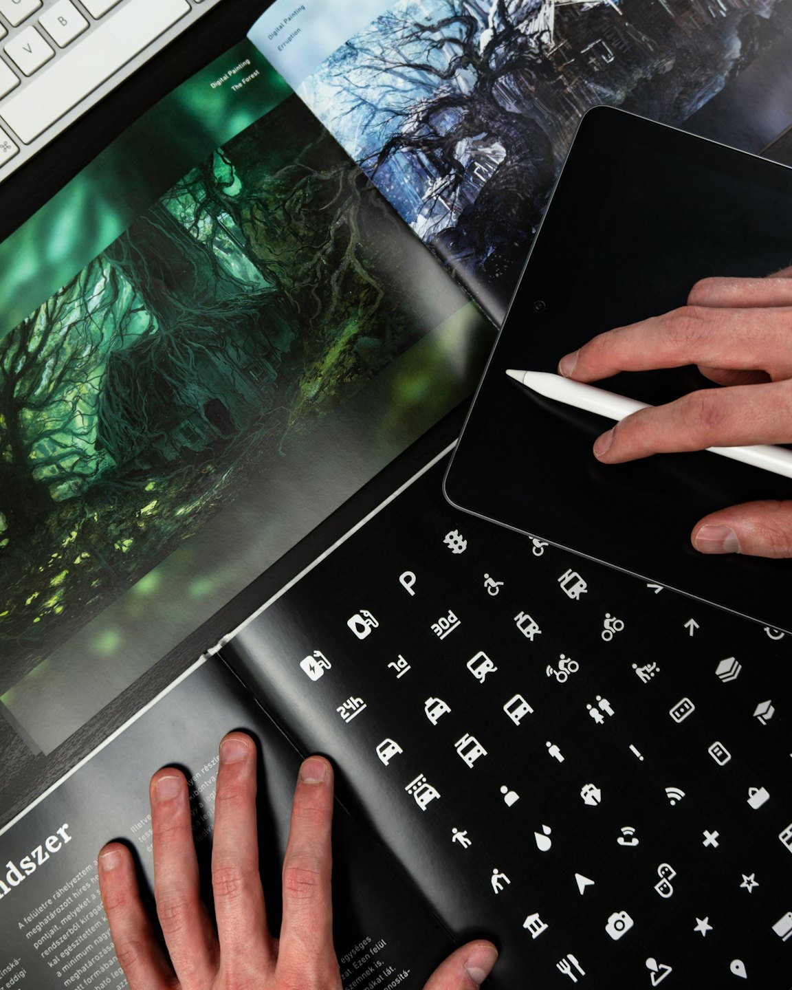 Mains utilisant un stylet sur une tablette à côté d'un magazine et d'un clavier.