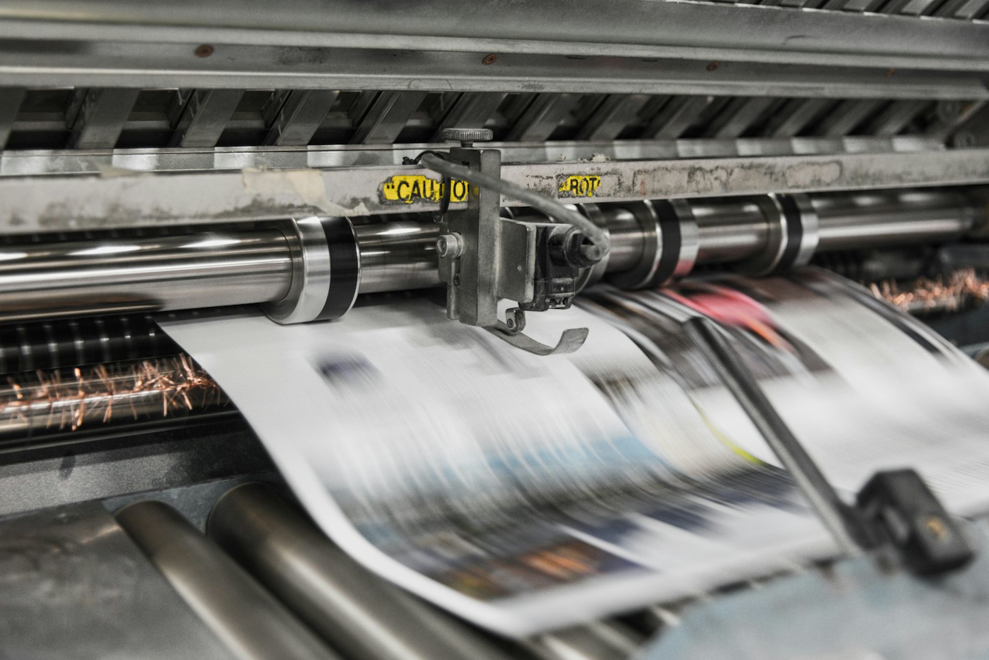 Presse d'imprimerie faisant passer du papier dans des rouleaux métalliques.