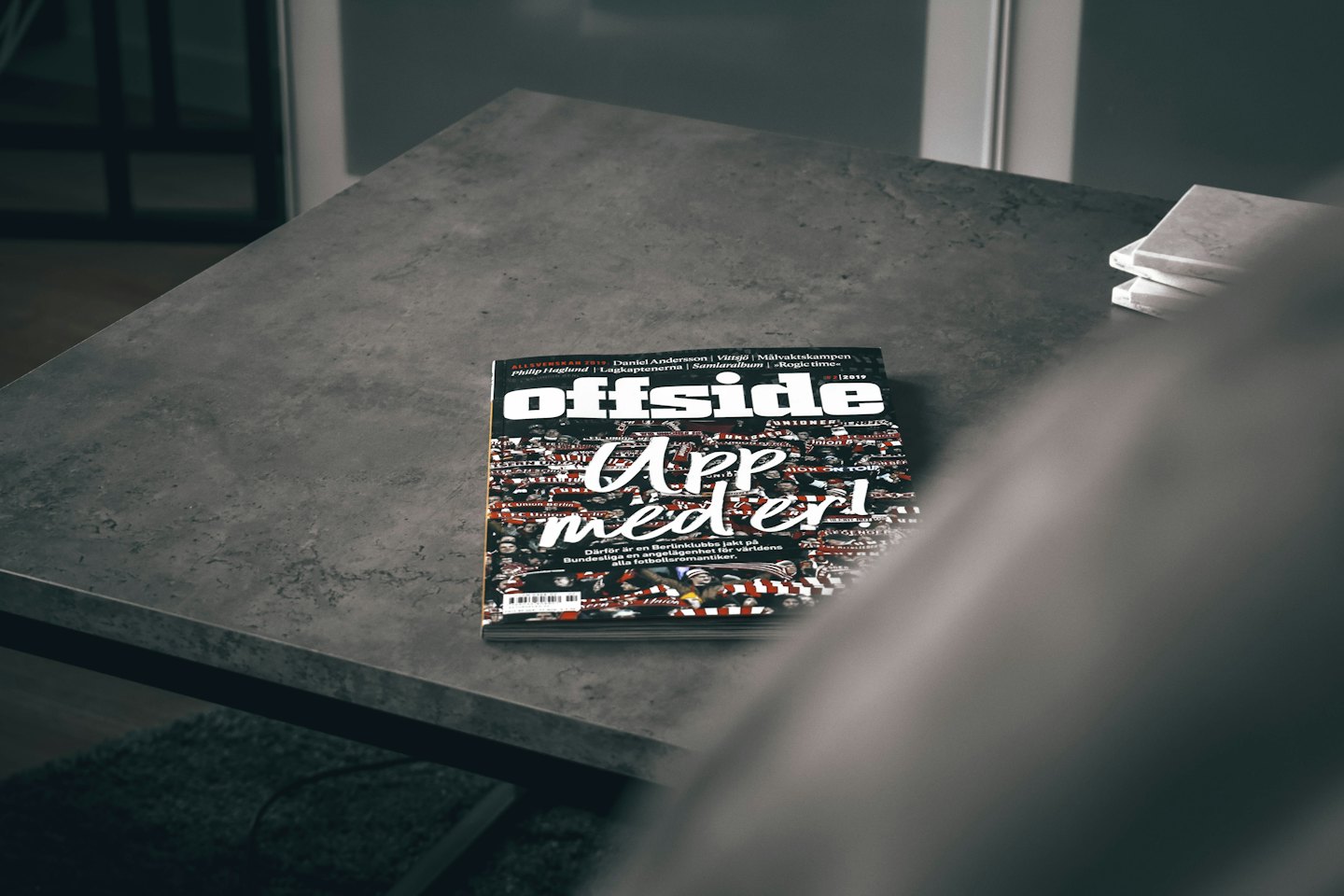 Un magazine Offside repose sur une table en béton à côté de sous-verres blancs.