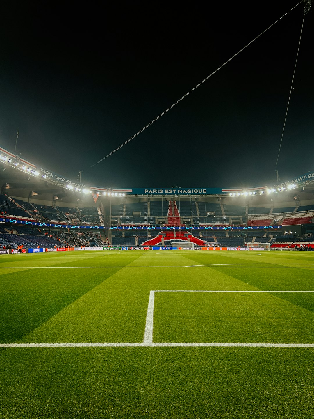 Terrain de football vide dans un stade la nuit, éclairé par de vives lumières.