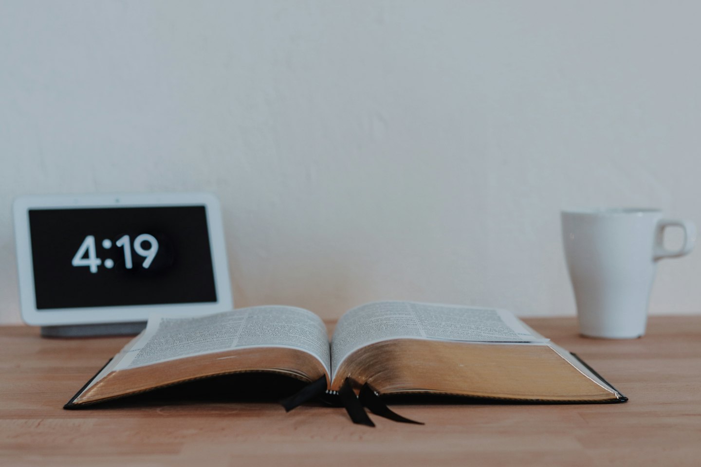Un livre ouvert, un écran numérique et une tasse sur une table.